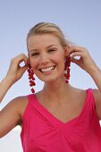 Blonde woman holding currant branches to her ears, smiling