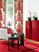 Living room with red floral print wall, table, chest of drawers, chair and cushion