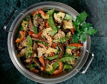 Stir fried vegetables with beef, sesame seeds, paprika, sugar peas and mushrooms in pot