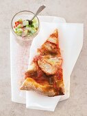 Piece of chicken tandoori pizza on folded tissue with cucumber and mint yoghurt