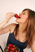 Portrait of woman with long hair eating strawberry, smiling, close-up