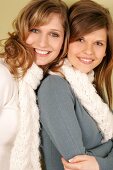 Portrait of two beautiful woman wearing sweater and scarf standing side by side, smiling