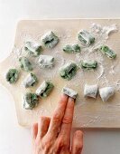 Rolling pieces of soft dough in flour with fingers on wooden board