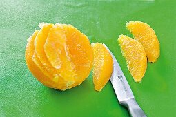 Close-up of orange slices with knife on green background