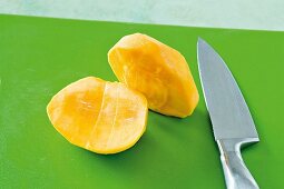 Close-up of halved mango with knife on green background