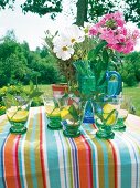 Glasses of lemon and mint with pink and white flowers in carafe on table