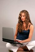 Beautiful woman with long curly hair in blue top sitting with laptop