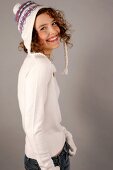 Portrait of beautiful woman with curly hair wearing white sweater and cap, smiling widely