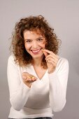 Portrait of beautiful woman with curly hair wearing white sweater holding pill, smiling