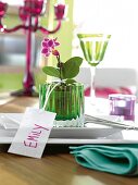 Green glass pot with purple mini orchid and name tag with 'Emily' for table decoration