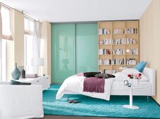 Bedroom in white and beige with blue double bed, bookcase and window