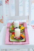 weiße Kerzen mit Blütenkranz auf rosa Tablett