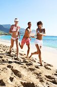 Zwei Frauen und ein Mann spielen am Strand mit einem Ball