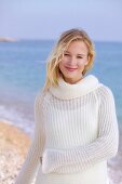 Portrait of beautiful blonde woman wearing white sweater standing on beach, smiling