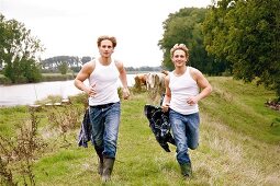 Two handsome men wearing white vest and jeans running on grass, smiling