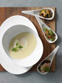 Potato soup in soup bowl and three spoons of topping on wooden board
