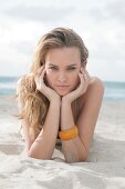 Portrait of beautiful blonde woman wearing brown top lying on beach, smiling