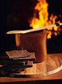 A stack of chocolate in front of a pot with an open fire in the background