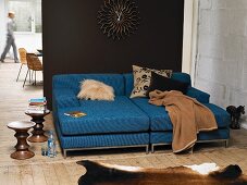 Blaues Sofa mit Kissen und Decke vor brauner Wand