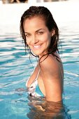 Portrait of beautiful brown eyed brunette woman wearing bikini in pool, smiling