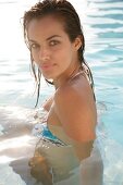 Frau mit brünetten Haaren, Bikini im Pool blickt in die Kamera