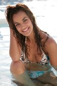 Frau mit brünetten Haaren, Bikini im Pool lacht in die Kamera