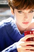 Portrait of green eyed woman with short hair in blue sweater holding red glass with drink