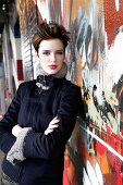 Portrait of pretty woman wearing black fur jacket standing with arms crossed against wall