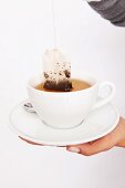 Teabag being dipped in teacup with saucer