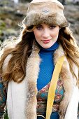 Beautiful woman with red long hair wearing fur cap and fur vest, smiling