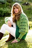 Portrait of beautiful blonde woman wearing green sweater sitting on grass