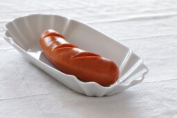 Boiled sausage on serving dish against white background