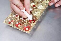 Person spraying cast spray on floral pattern marzipans in moulding tray