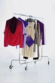 Several clothes in vibrant colours hanging on clothes rack against white background