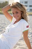 Portrait of pretty blonde woman wearing zipper jacket sitting on beach, smiling