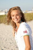 Portrait of young blonde woman wearing white zipper standing on beach, smiling
