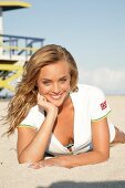 Portrait of pretty blonde woman wearing white zipper lying on beach, smiling