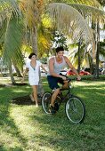 Young couple having fun, man riding bicycle and woman running behind him