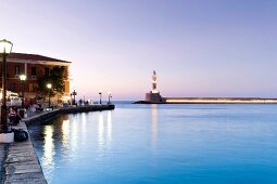 Chania Lighthouse at dawn and people sitting on bench at promenade near sea, Crete, Greek