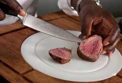 Close-up of man's hand chopping fillet with knife on plate