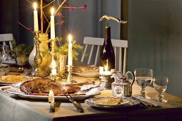 Table laid with venison, red wine, sauce, burning candle and champagne bottle