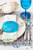 A maritime place setting with a blue stemmed glass on a raffia placemat