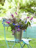 Sommerblumen in einem Metalleimer auf einem Gartenstuhl