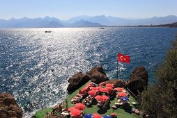 Turkish flag and people relaxing on sun loungers near sea in Antalya, Turkey