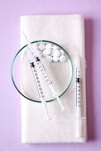 Close-up of three syringes and tablets kept in bowl and white napkin