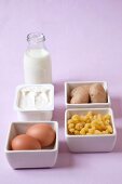 Bottle of milk, egg, potatoes, pasta and butter in serving dish against pink background