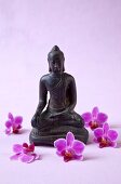 Close-up of Buddha statue surrounded by orchid flowers