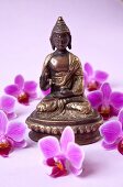 Close-up of Buddha statue surrounded by orchid flowers