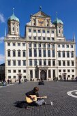 Man playing guitar in front of Augsburg Town Hall in Augsburg, Bavaria, Germany