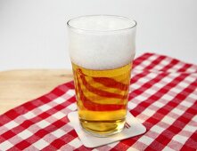 Glass of beer with froth on red and white checked table cloth